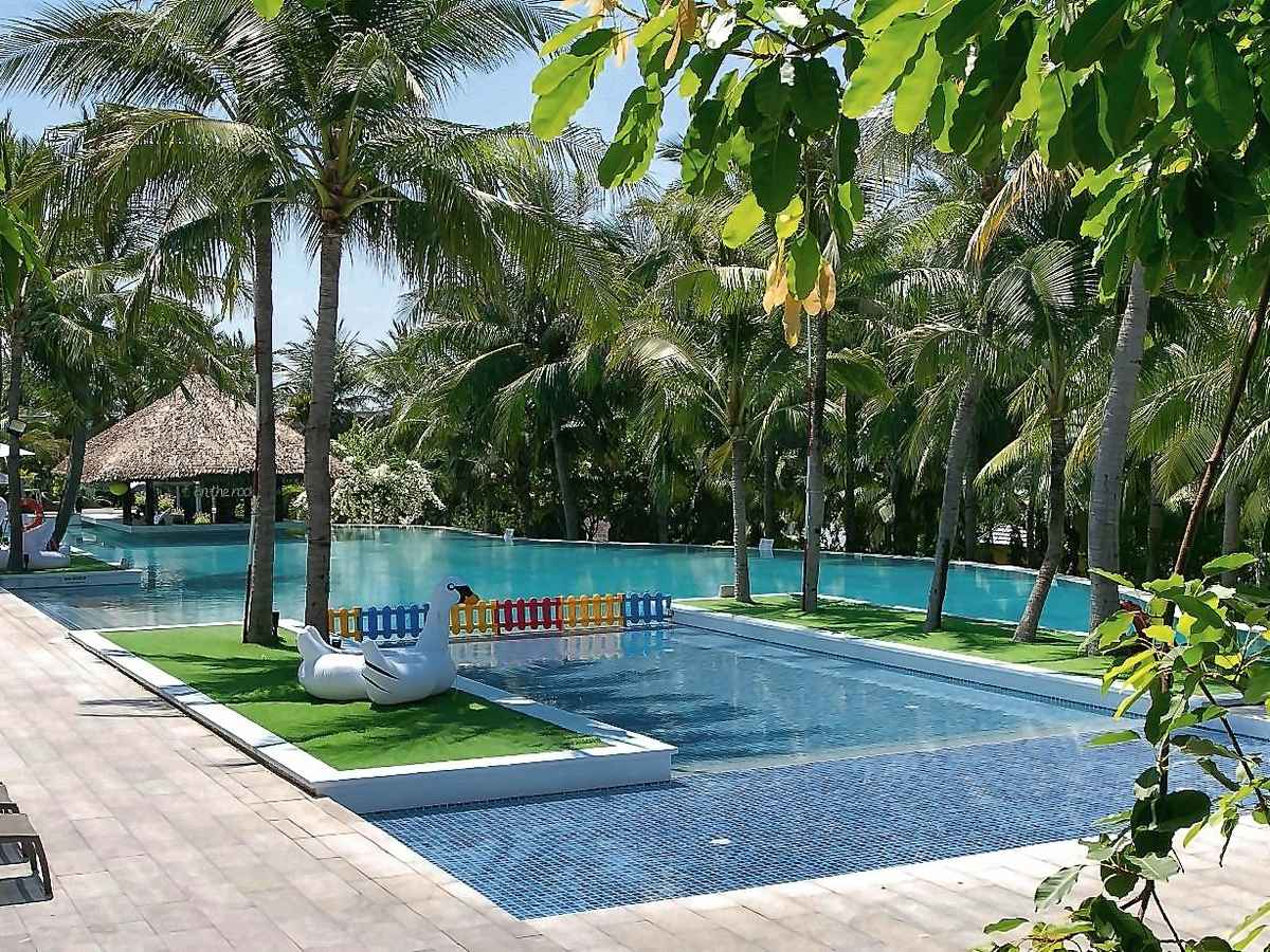Pool lined with palm trees and loungers, with a thatched shelter at the far end