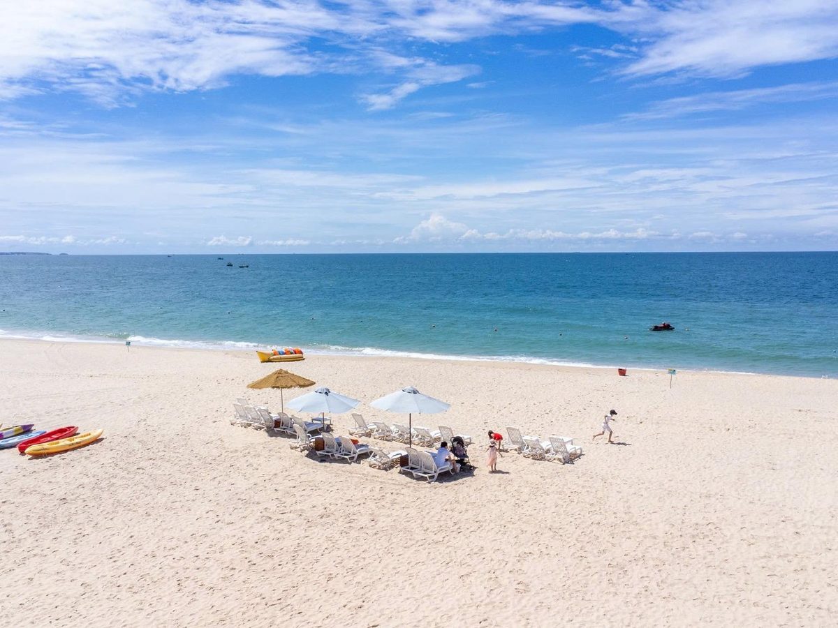 Wide beach with white umbrellas, loungers and kayaks lined up on the sand