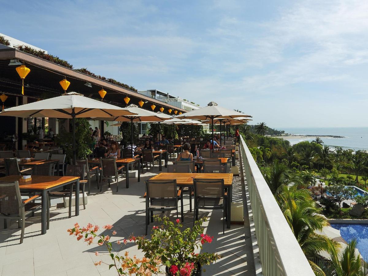 Restaurant terrace with tables under umbrellas, looking over gardens to the sea
