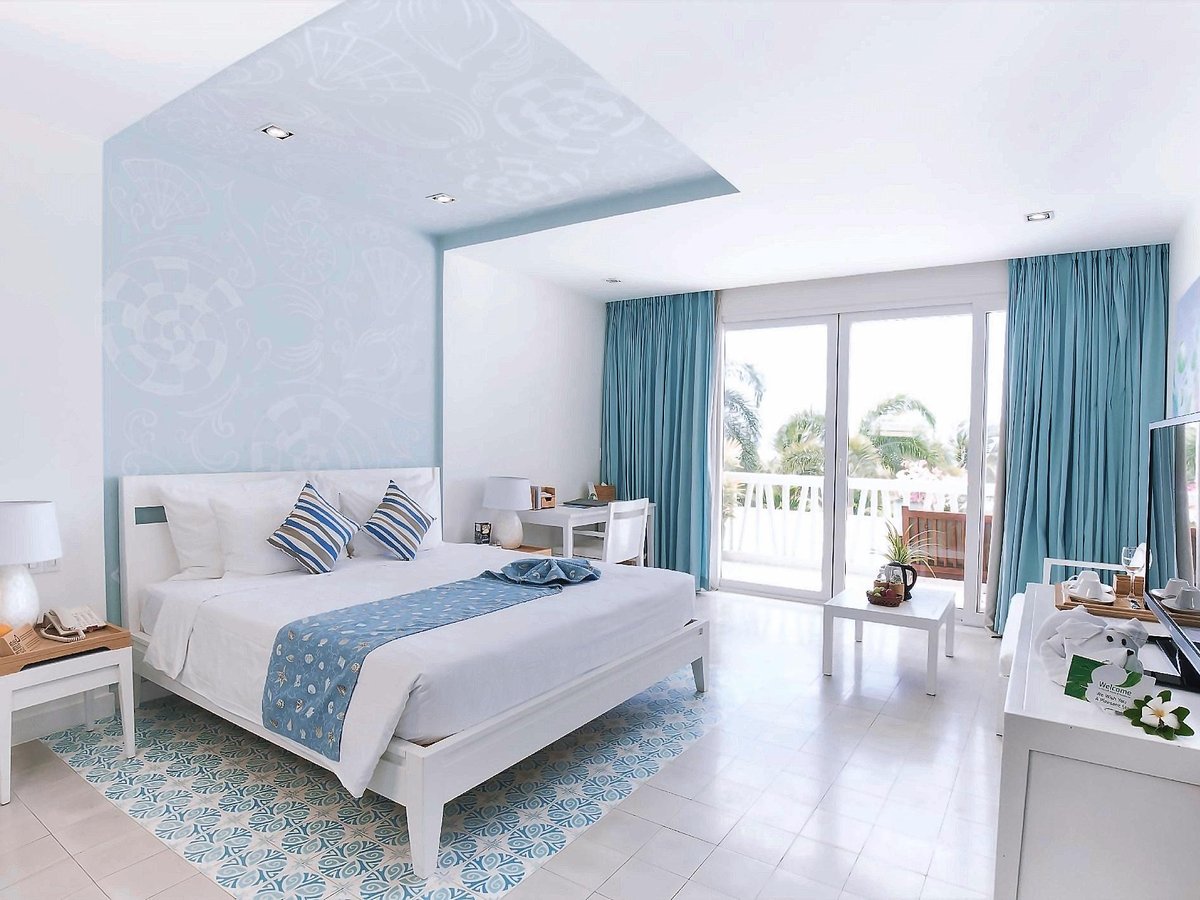 Room with a large bed under a blue patterned ceiling panel and glass doors to a balcony