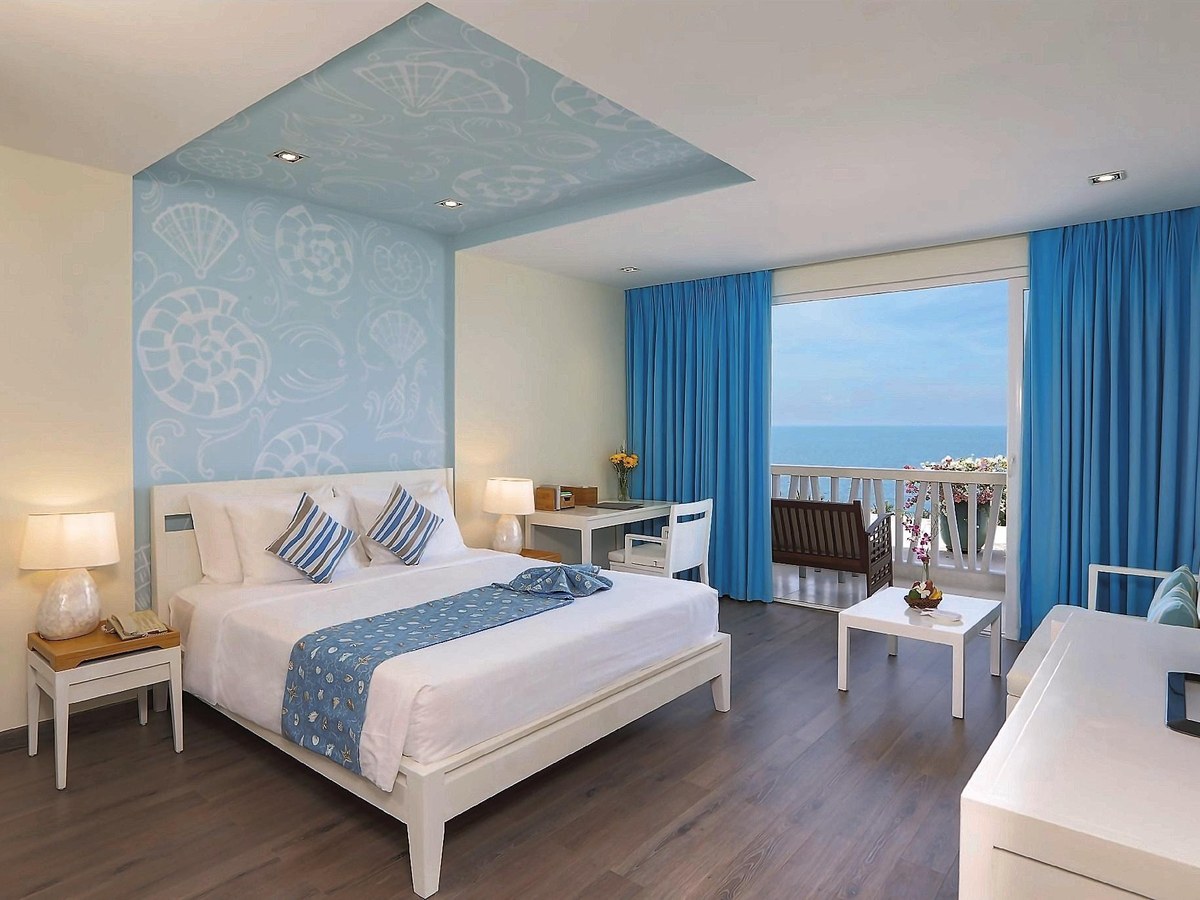Bright room with a large bed, blue curtains and a balcony door open to the sea