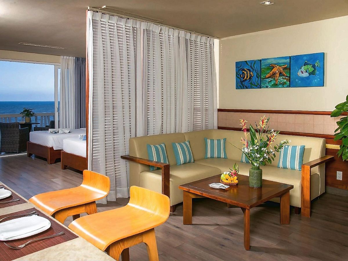 Open living area with a sofa, dining table and twin beds beyond, sea through the windows