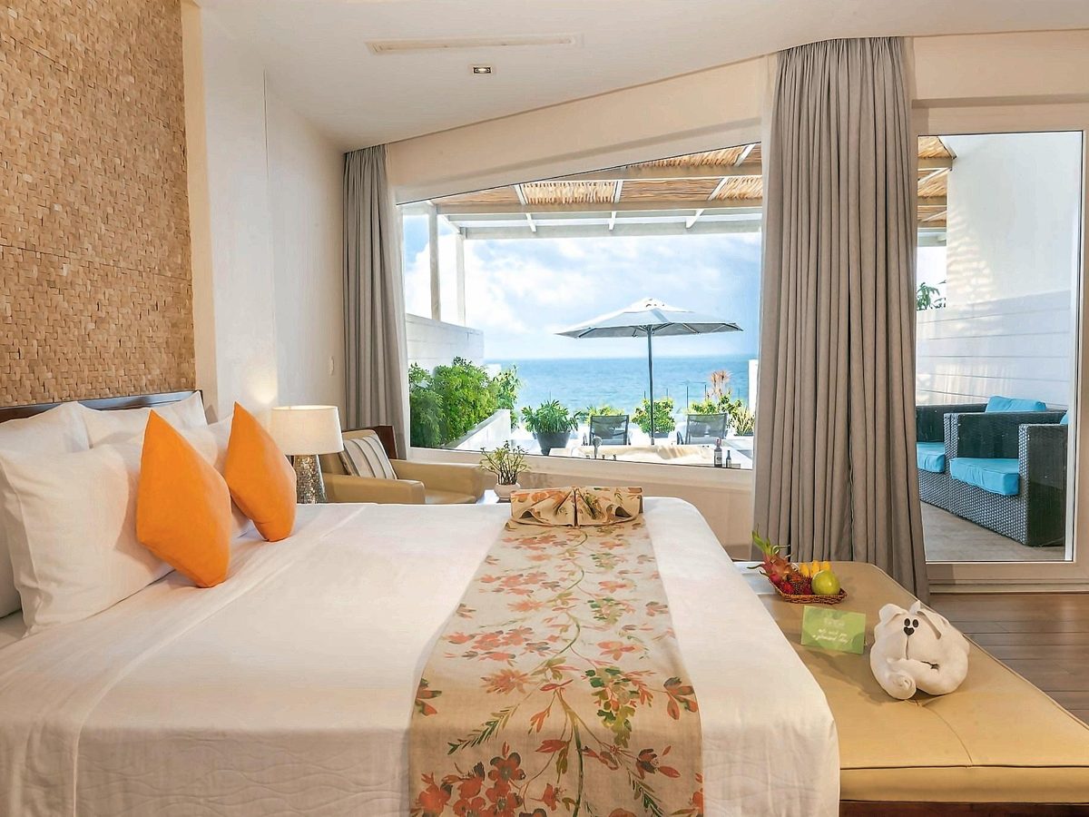 Bedroom with orange cushions and a glass wall opening onto a terrace with sea views