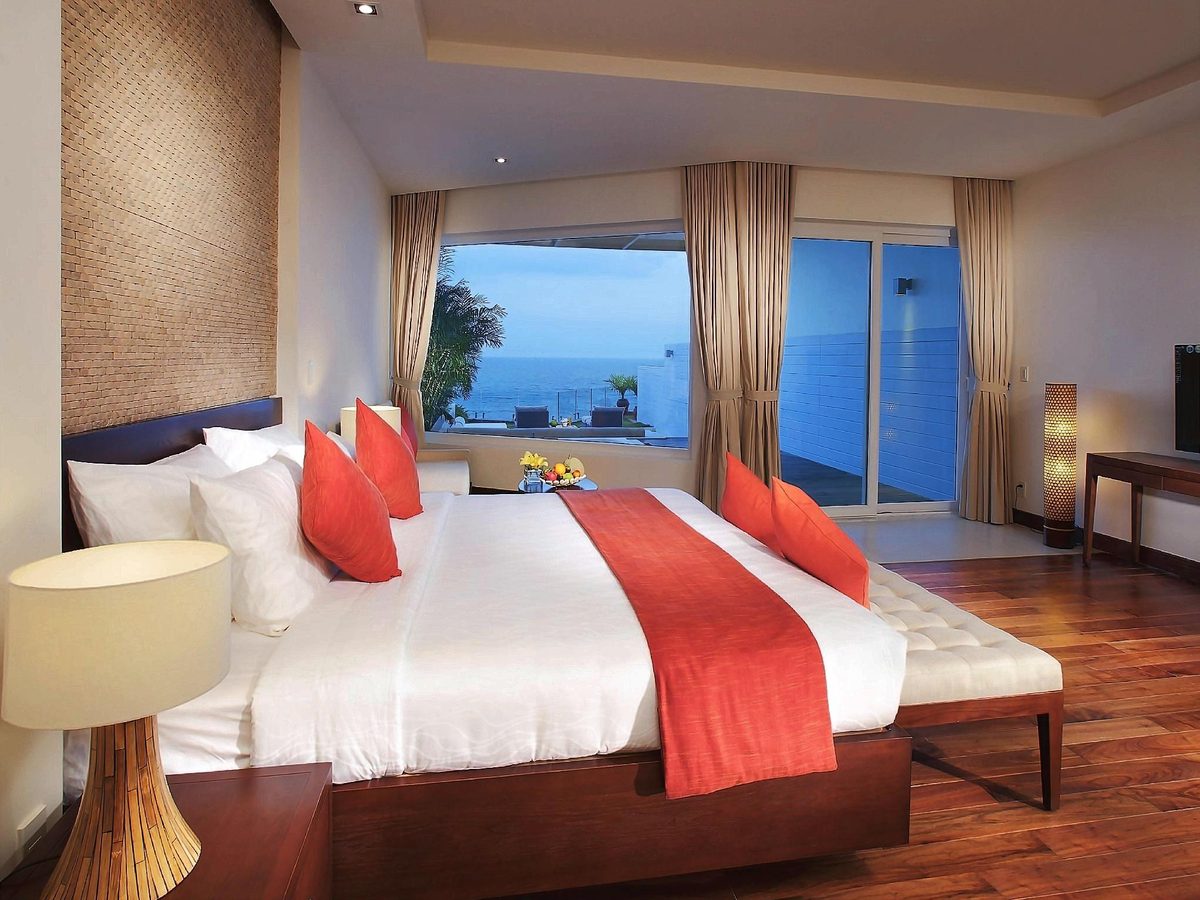 Bedroom with a red runner on white bedding and a window framing the sea