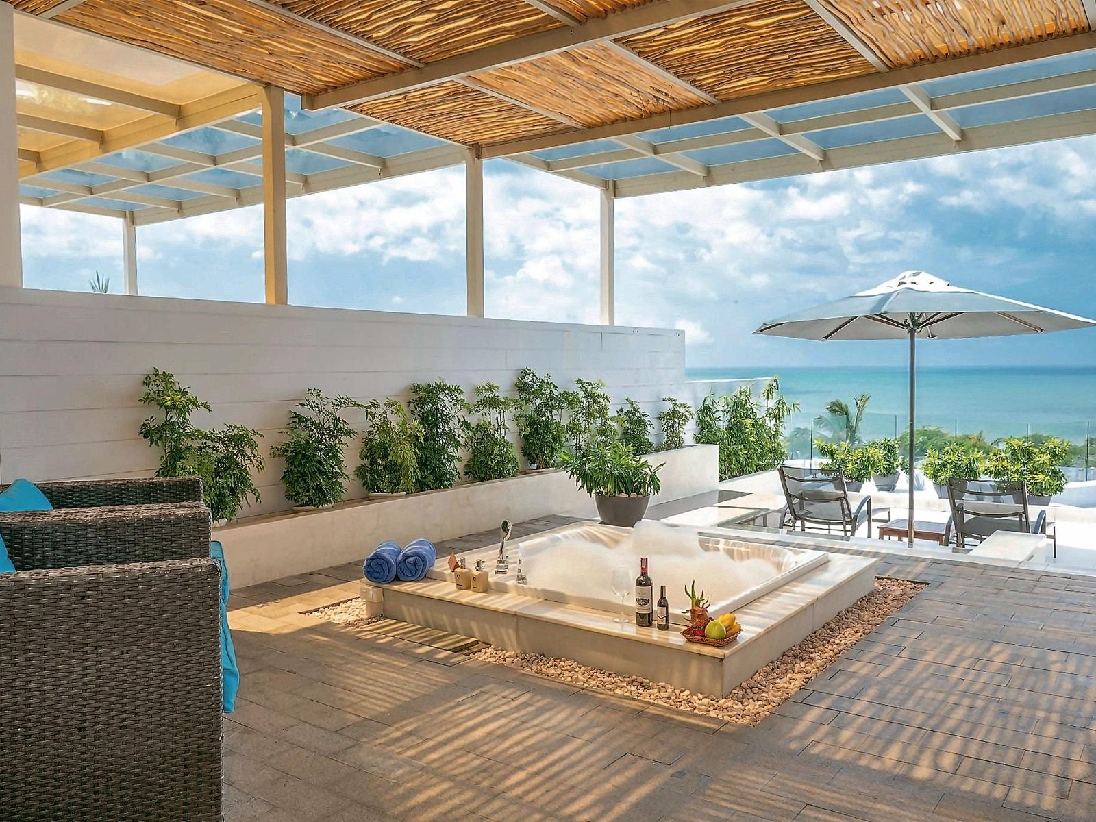 Covered terrace with a sunken hot tub, rattan chairs and a wide view of the sea