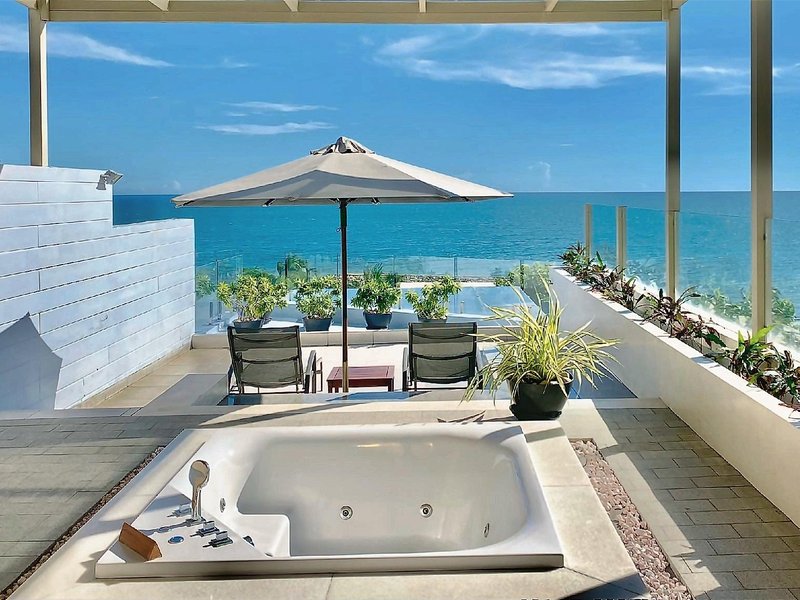 Outdoor hot tub on a sunny terrace with loungers, an umbrella and the sea beyond